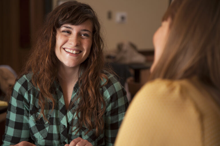 Two beautiful young women sit together and talk.